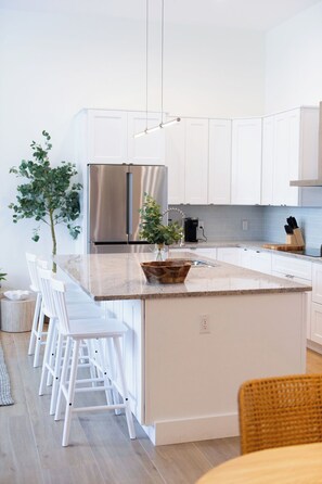 A modern kitchen with white cabinets, stainless steel appliances, a central island with stools, and a hanging light fixture. - Rosemary District Flat in Downtown Sarasota 3 (Sarasota)