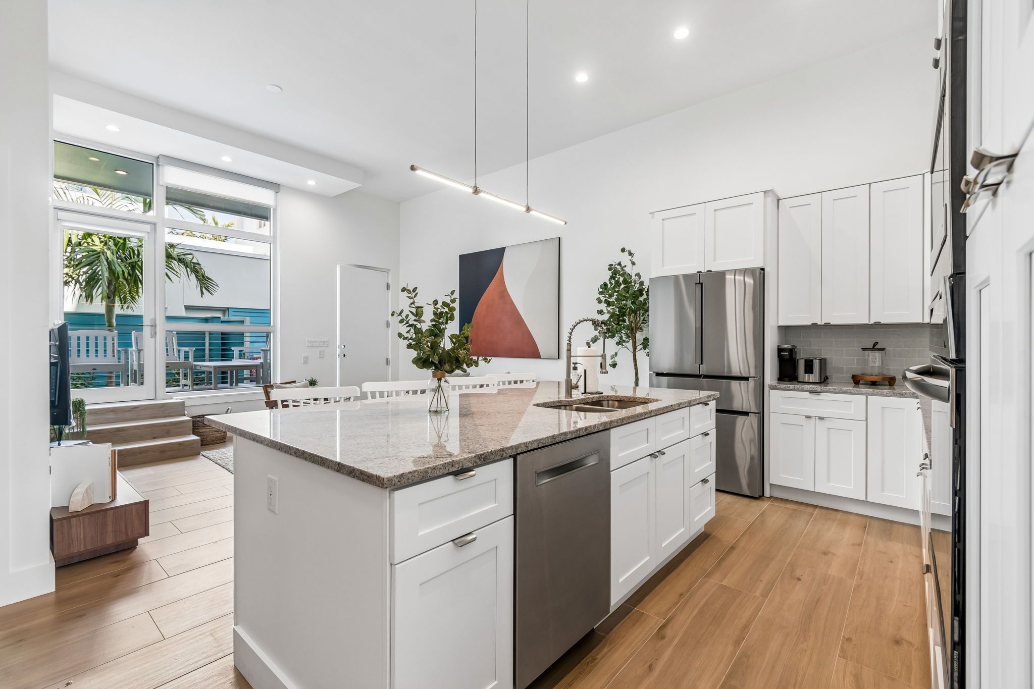 A modern kitchen with white cabinetry, a stainless steel refrigerator, and a large island with a dishwasher.