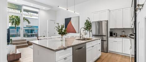 A modern kitchen with white cabinetry, a stainless steel refrigerator, and a large island with a dishwasher.