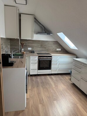 Une cuisine moderne dotée d’un puits de lumière, d’un four encastré et de meubles de rangement blancs.