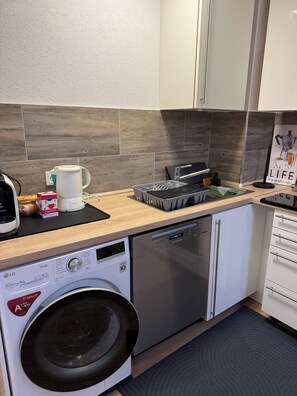 Une cuisine compacte équipée d’un lave-linge, d’un lave-vaisselle et d’une machine à café posée sur le plan de travail.