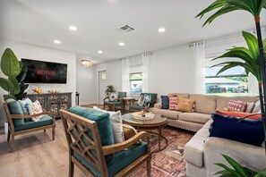 Ein Wohnzimmer mit Fernseher, Sofas, Sesseln, einem Couchtisch und einer großen Pflanze.