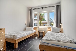 Ein Zimmer mit zwei Holzbett, einem kleinen Tisch, einer Heizung und einem Fenster mit Vorhängen.