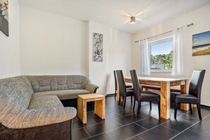 Ein modernes Wohnzimmer mit einem grauen Ecksofa, einem Holztisch und einem Essbereich mit einem Holztisch und schwarzen Stühlen.