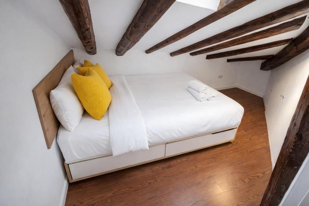 Una cama individual con ropa de cama blanca, un almohadón amarillo y una toalla blanca en el suelo.