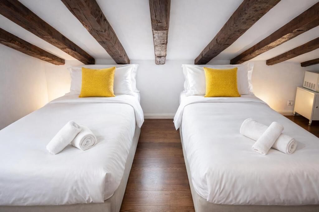 Une chambre avec deux lits, des poutres en bois, du linge de lit blanc et un oreiller jaune.