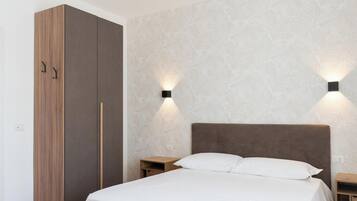 A bedroom with a bed, wooden wardrobe, and two nightstands with wall-mounted lights.