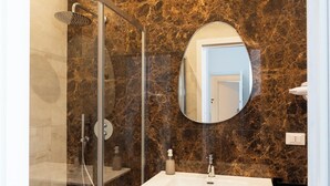 Un baño con ducha envuelta en cristal, un lavabo, un espejo y una pared de mármol.