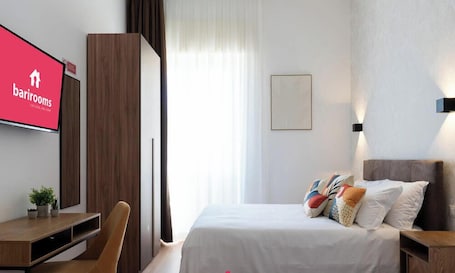 A hotel room with a bed, a desk, a chair, a TV, and a window with curtains.. Barirooms - Lungomare