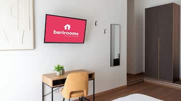 Een moderne hotelkamer met een houten bureau, een stoel, een potplant, een aan de muur bevestigde televisie, een spiegel en een garderobe.