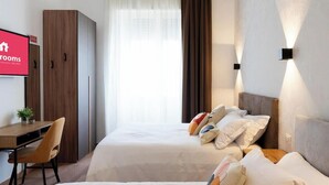 Habitación de hotel con cama, escritorio, armario y televisor mostrando el nombre del hotel.
