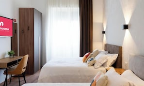 Hotellihuone, jossa on sänky, työpöytä, vaatekaappi ja televisio, jossa näkyy hotellin nimi.