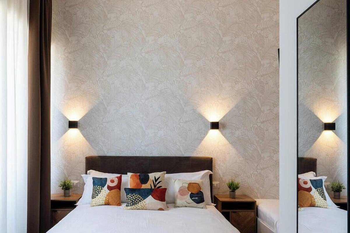 Habitación de hotel con una cama grande, dos mesitas de noche, un tocador, un espejo y una pared con diseño.