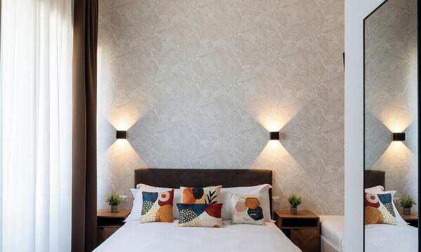 Habitación de hotel con una cama grande, dos mesitas de noche, un tocador, un espejo y una pared con diseño.