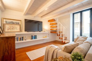 Ein modernes Wohnzimmer mit Holzboden, einer Couch, einem Fernseher, Bücherregalen und einer Treppe.