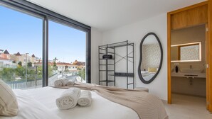 A hotel room with a large bed, a view of the city, a bathroom with a mirror and sink, and a shelf with towels.