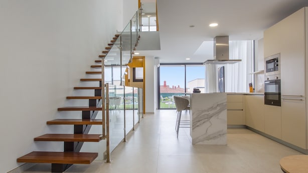A modern kitchen with a marble island, stainless steel appliances, and a glass staircase.