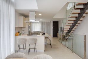 A modern kitchen with a central island, bar stools, and a staircase with glass railings.
