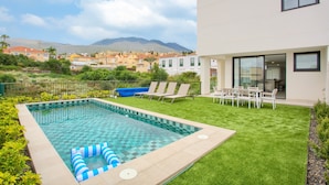 A swimming pool with a checkered pattern, surrounded by a well-maintained lawn and lounge chairs.