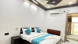 A bedroom with a bed, nightstand, air conditioning unit, and a window with curtains. - Vidya Dham Vrindavan  (Vrindavan)