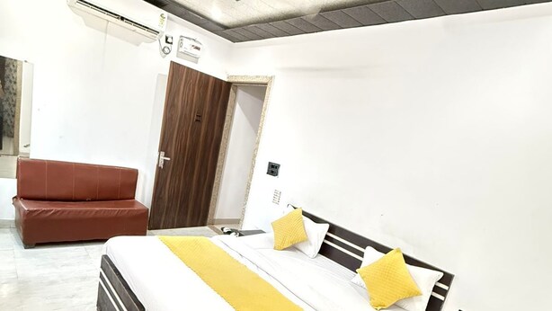 A bedroom with a bed, a brown leather chair, a wooden door, and a ceiling fan. - Vidya Dham Vrindavan  (Vrindavan)