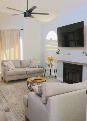 Ein Wohnzimmer mit einer Couch, einem Couchtisch, einem Kamin und einem an der Wand befestigten Fernseher.