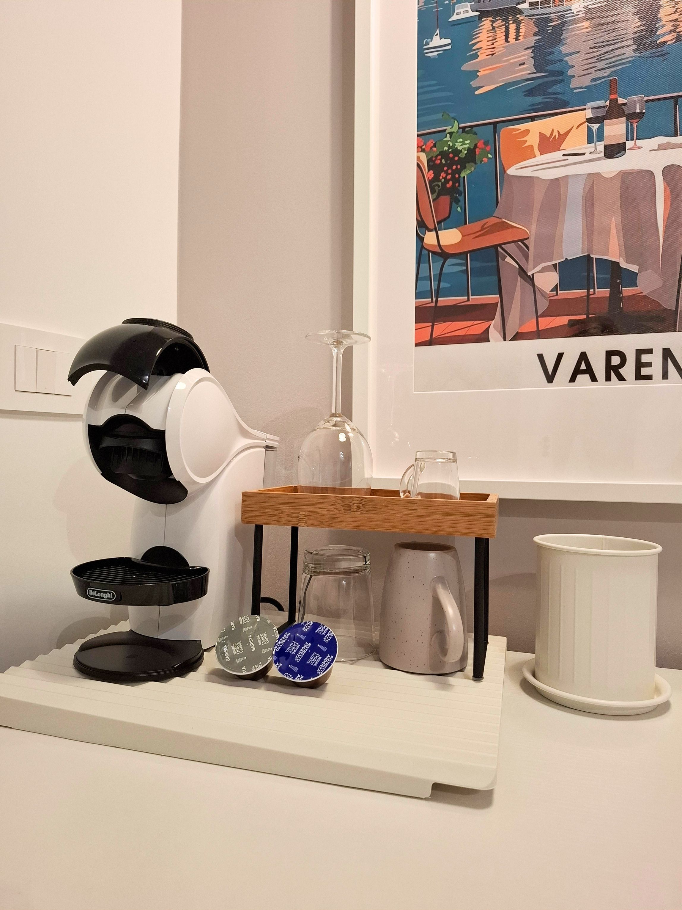 Una cafetera, un tarro de cristal, una taza y un recipiente blanco sobre un estante blanco.