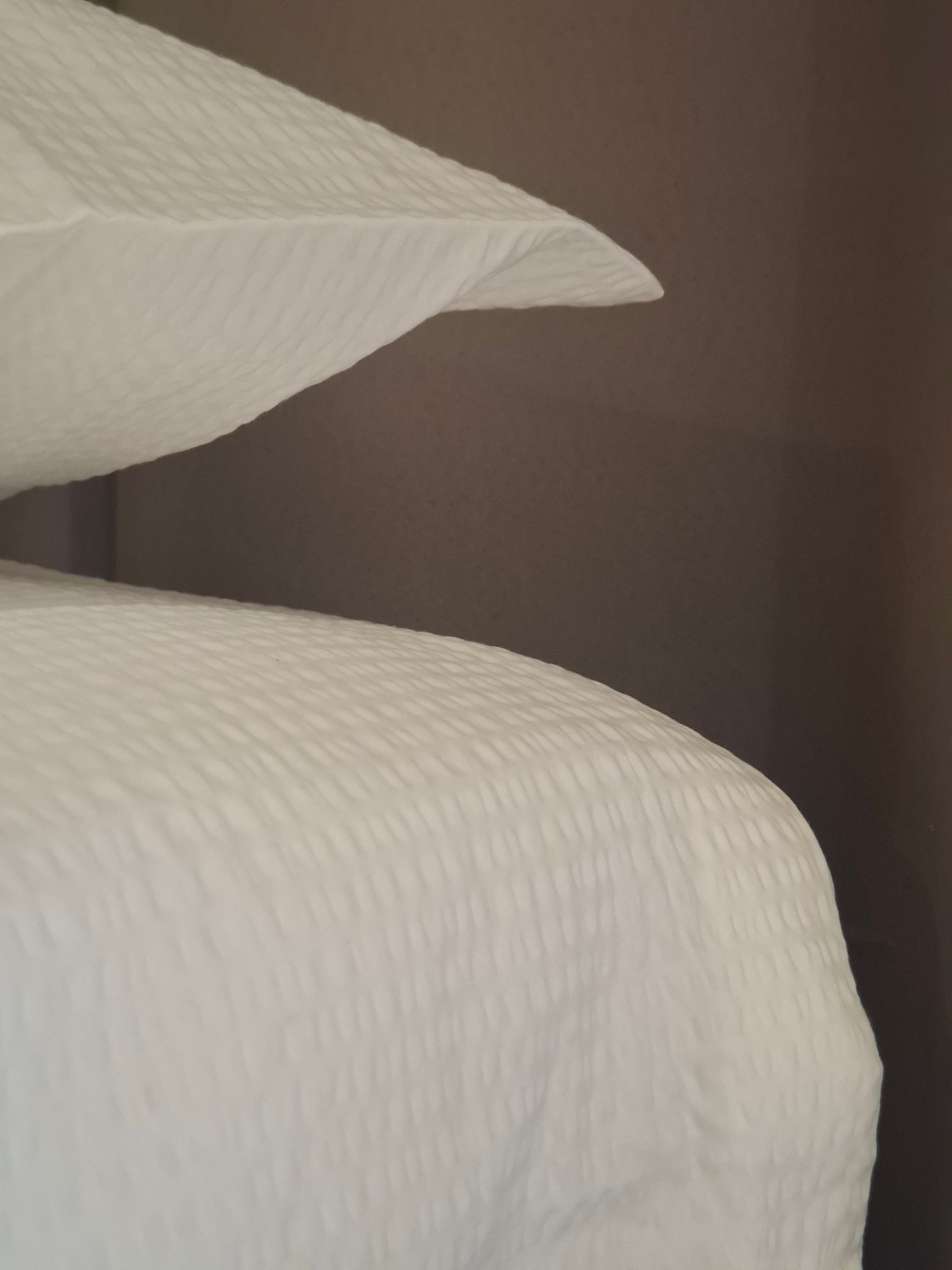 Ein Bett mit einer gewölbten weißen Bettdecke und einer dunklen Wand im Hintergrund.