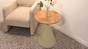A room with a beige armchair, a small wooden table with a vase of flowers, and a hanging light fixture. - Eva Urban Rooms Centro Lecco (Lecco)