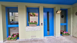 A building entrance with blue doors, a window with a flower box, and a paved area. - Eva Urban Rooms Centro Lecco (Lecco)