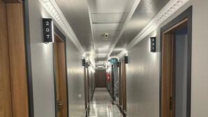 Un pasillo de hotel con suelo de mármol, puertas de madera y placas con los números de las habitaciones.