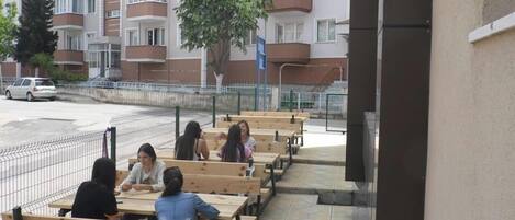 Outdoor wooden benches arranged in rows, a paved walkway, and a multi-story residential building in the background.