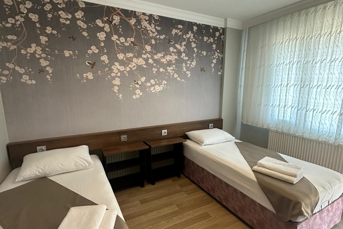 Habitación de hotel con dos camas, un mural floral en la pared, una ventana con cortinas e iluminación en el techo.