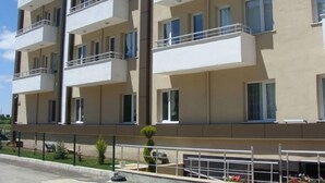Un edificio residencial de varios pisos con balcones, entrada protegida por un portón y un pequeño jardín.