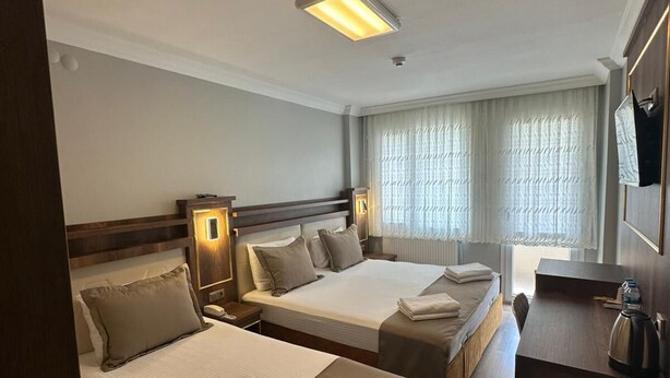 Habitación de hotel con dos camas, un escritorio, una cafetera y un ventanal grande con cortinas.