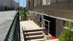 Un edificio con una escalera que conduce a un acceso cubierto, una valla verde y una fila de plantas en macetas.