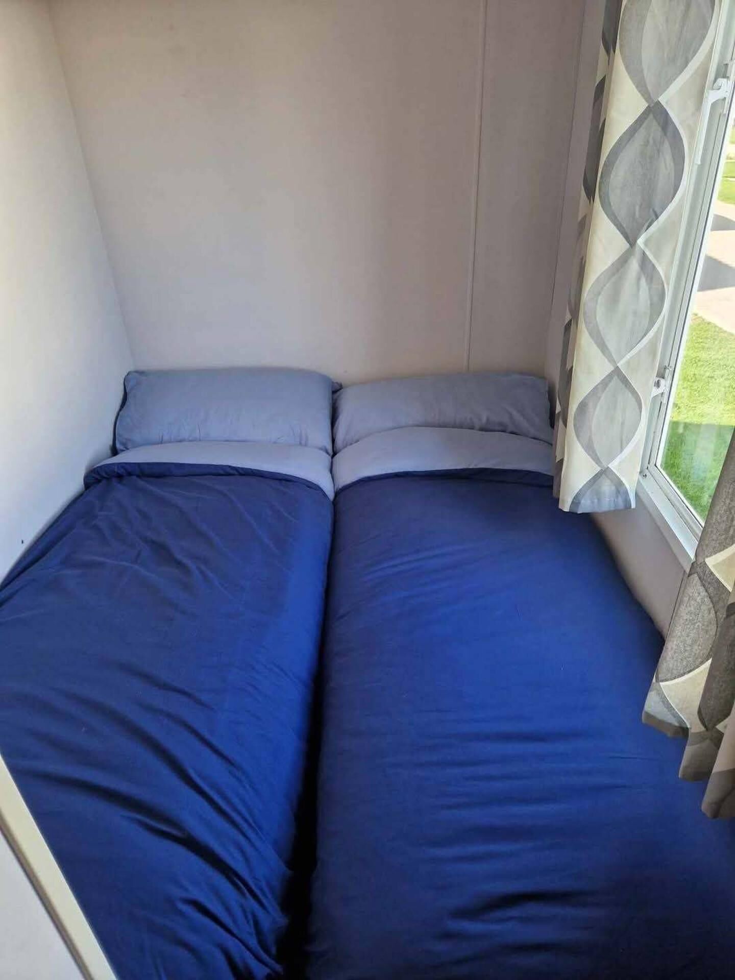 Una cama pequeña con ropa de cama azul en una habitación con ventana.