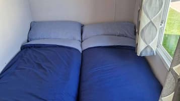 Una cama pequeña con ropa de cama azul en una habitación con ventana.