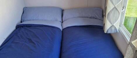 A compact bed with blue bedding in a room with a window.