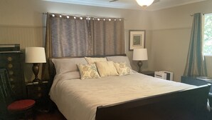 Ein Schlafzimmer mit einem Bett, zwei Nachttischlampen, einem Nachttisch, einer Kommode, einem roten Sessel und einem Deckenventilator.