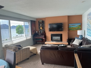 A living room with a fireplace, a television, and a view of a lake.