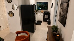 Eine kompakte Küche mit einem schwarzen Kühlschrank, weißen Schränken, einem Esstisch mit Pflanze und einem Fenster mit Aussicht.