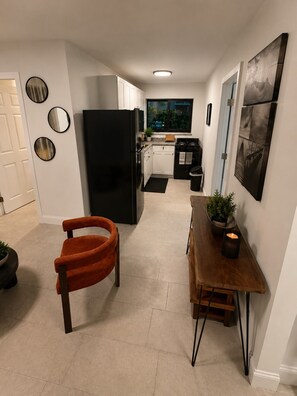 A compact kitchen with a black refrigerator, white cabinets, a dining table with a plant, and a window with a view. - 418 Luxury - Living 2 (Miami)
