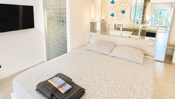 Ein modernes Schlafzimmer mit einem großen Bett, einem Flachbildfernseher und einem Badezimmer mit Spiegel und Waschbecken.