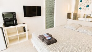 Ein modernes Hotelzimmer mit Bett, Flachbildfernseher, Mikrowelle und Schminktisch mit Spiegel.