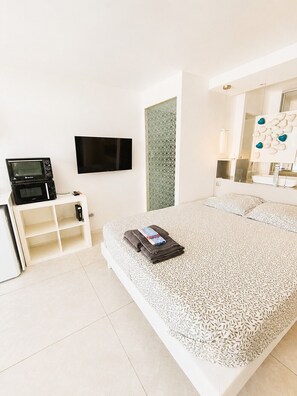 Quarto de hotel moderno com uma cama, televisão de tela plana, micro-ondas e toucador com espelho.