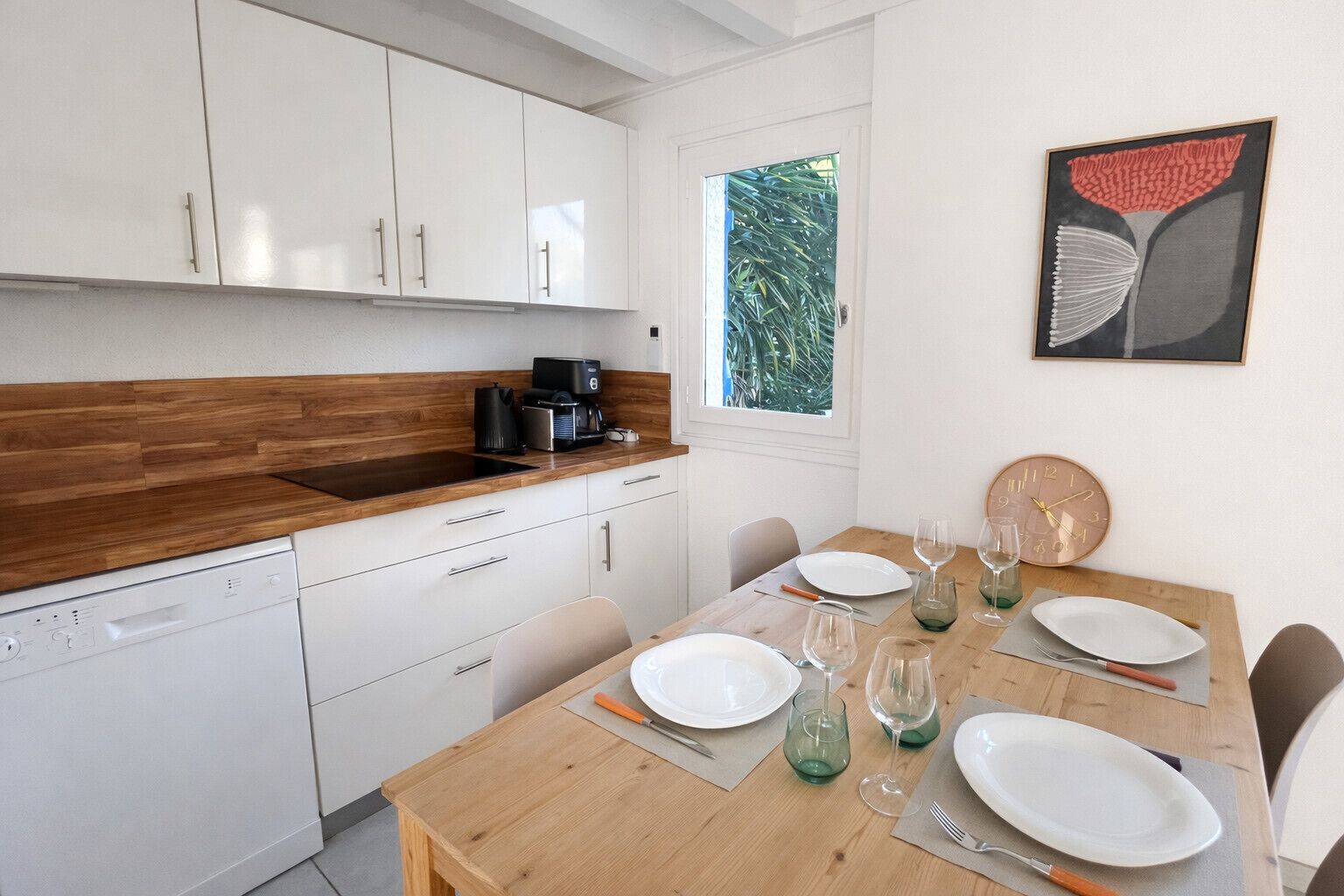 Una cucina moderna con mobili bianchi, un piano di lavoro in legno e un'area pranzo con un tavolo apparecchiato per due persone.