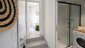 Un corridoio che conduce a una camera da letto con un letto, una lavatrice e un box doccia in vetro.