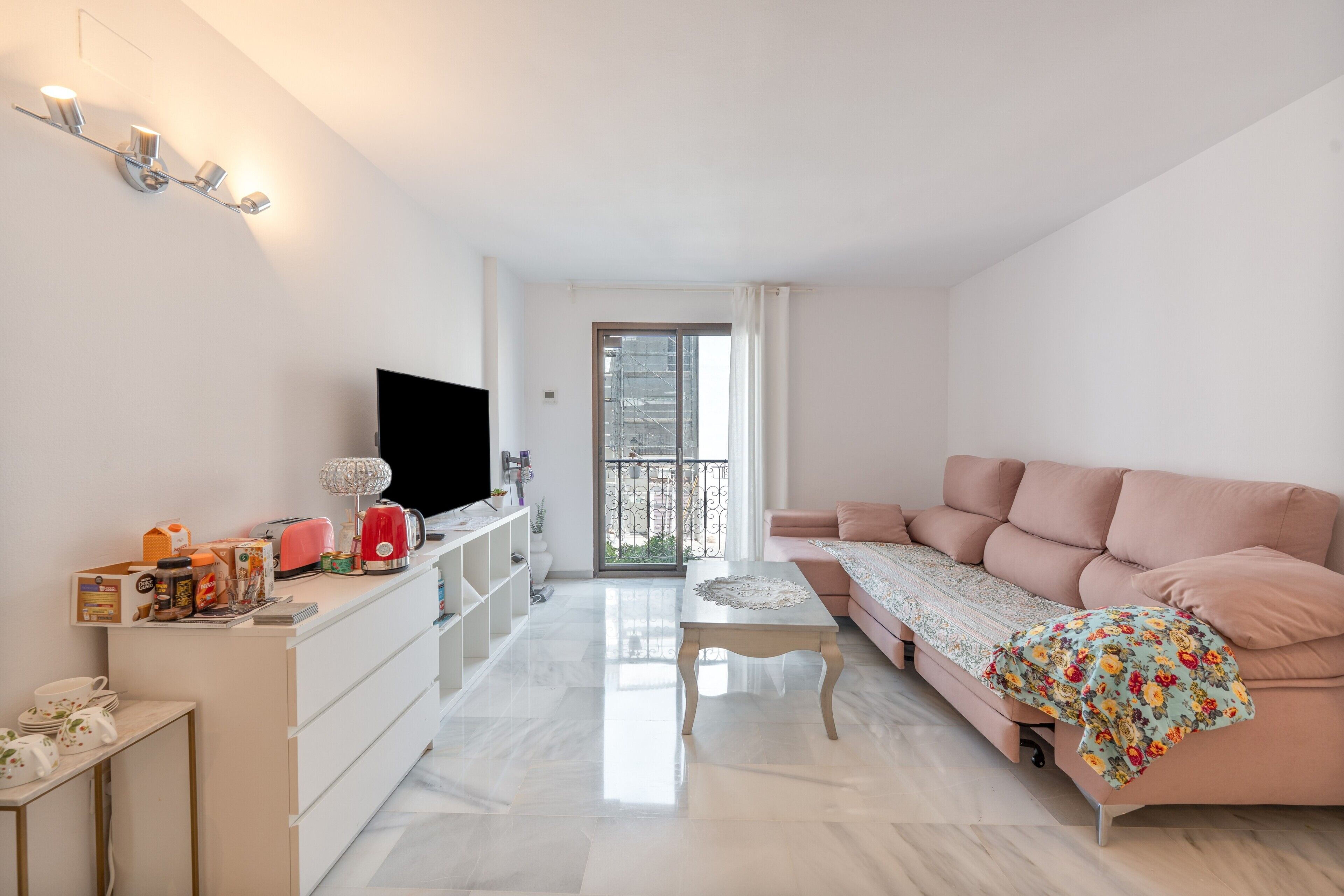 A modern living room with a sofa, a coffee table, a TV, and a balcony with a view.