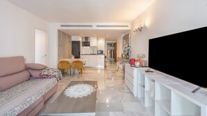 A modern living room with a sofa, a coffee table, and a TV. There is a kitchen in the background with a dining area. - Holiday Home 'Enjoy Puerto Banus Next To Beach' with Sea View, Wi-Fi and Air Conditioning (Marbella)